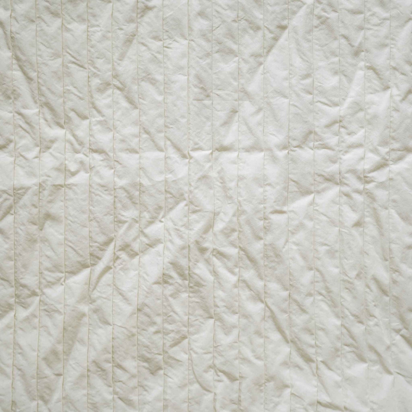 A white cushion with an elegant pleated design adds texture and style to any bedding arrangement.