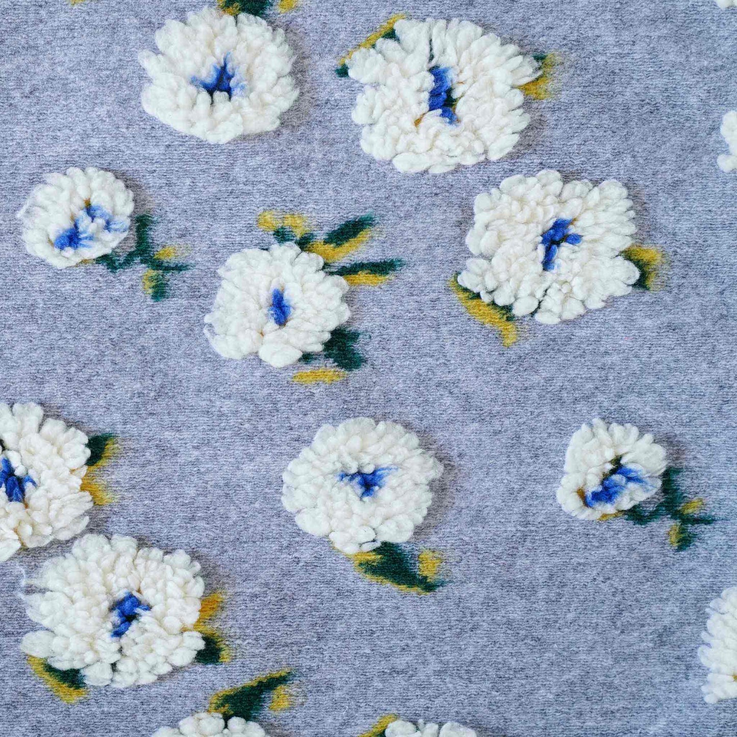 Embellished with delicate tufted white flowers in a soft textured gray cushion cover.