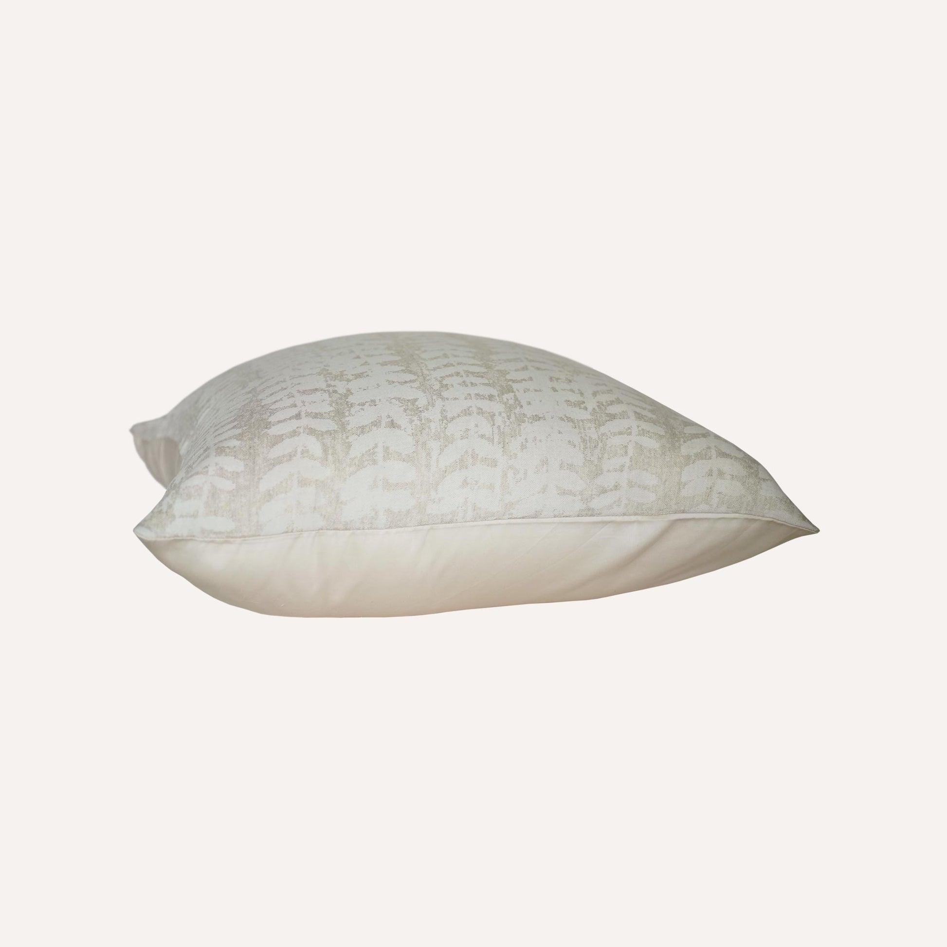 Square beige cushion with a subtle, textured leaf pattern on a plain background.