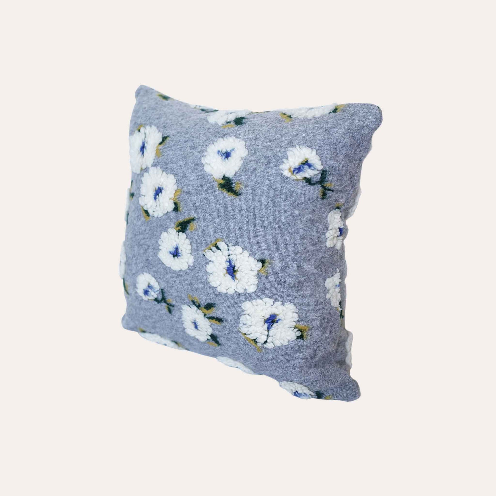 Embellished with delicate tufted white flowers in a soft textured gray cushion cover.
