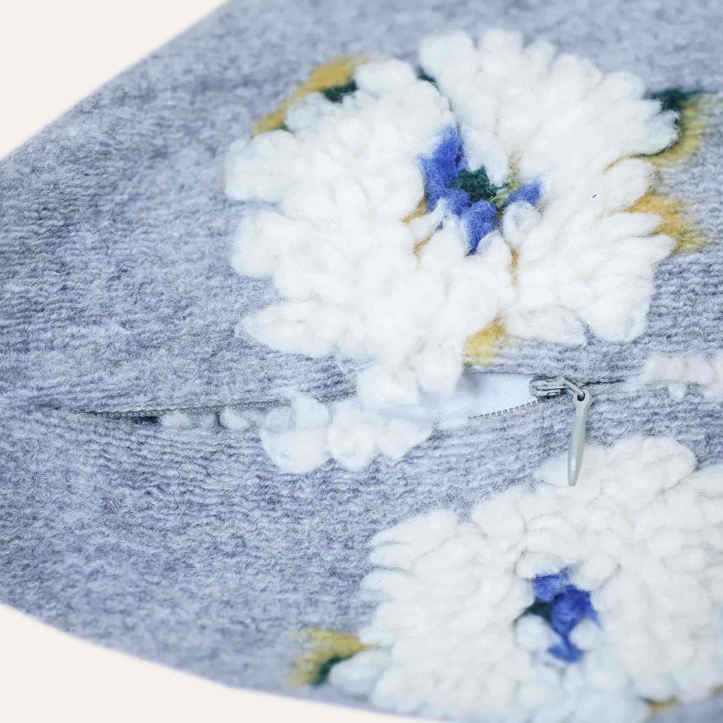 Embellished with delicate tufted white flowers in a soft textured gray cushion cover with invisible zipper.