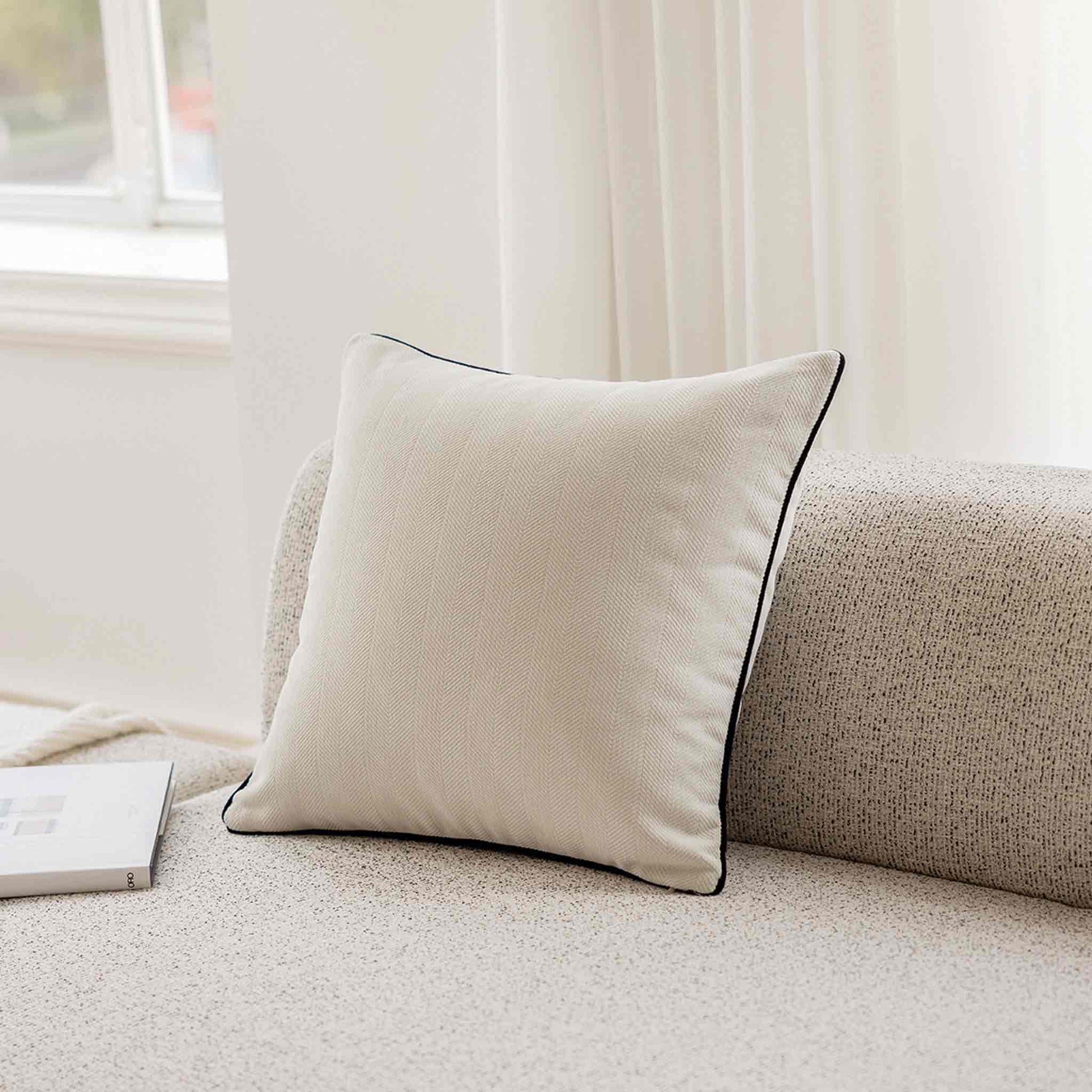 A stylish white cushion cover with black piping, designed with a herringbone texture on grey sofa.