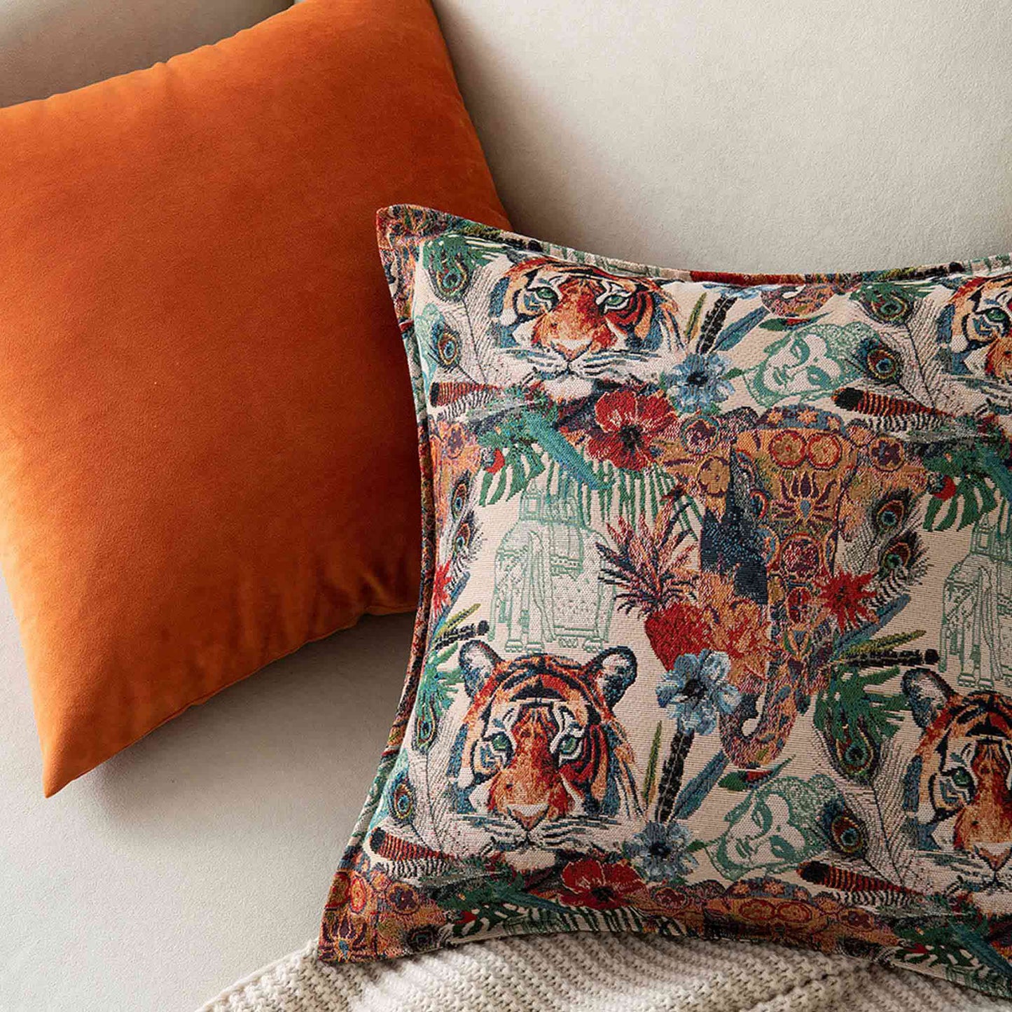 A bright orange cushion and a brightly colored tiger jacquard cushion on white sofa.