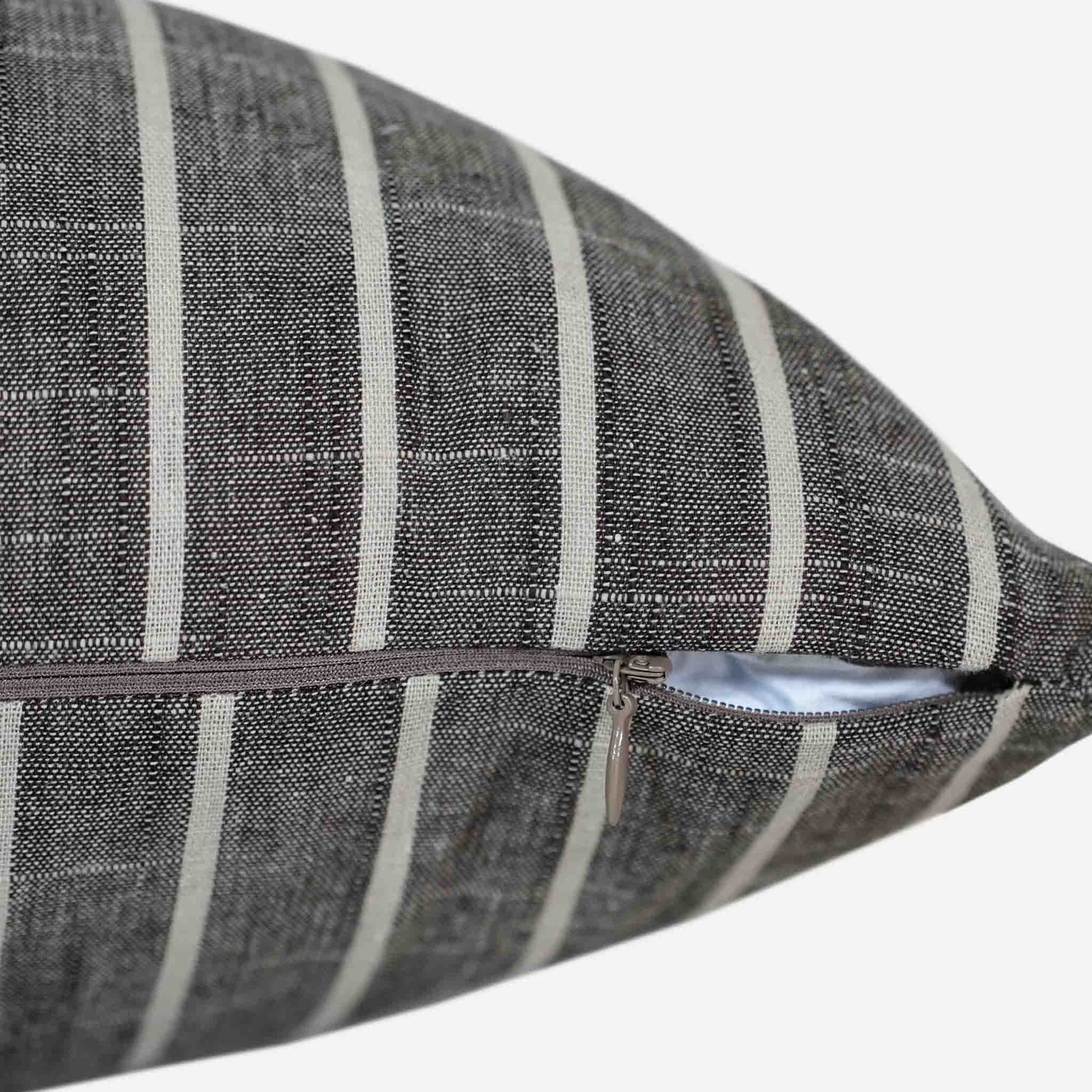 Close-up of the invisible zip on the white striped cushion on a grey background.