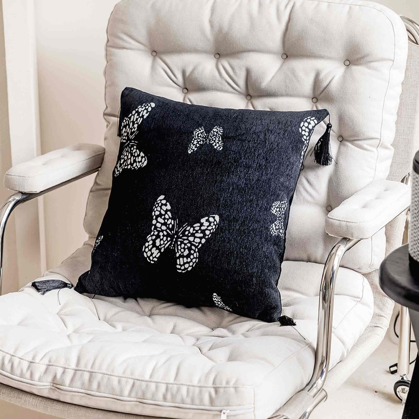 White butterfly on black background, fringed chenille cushion on chair.
