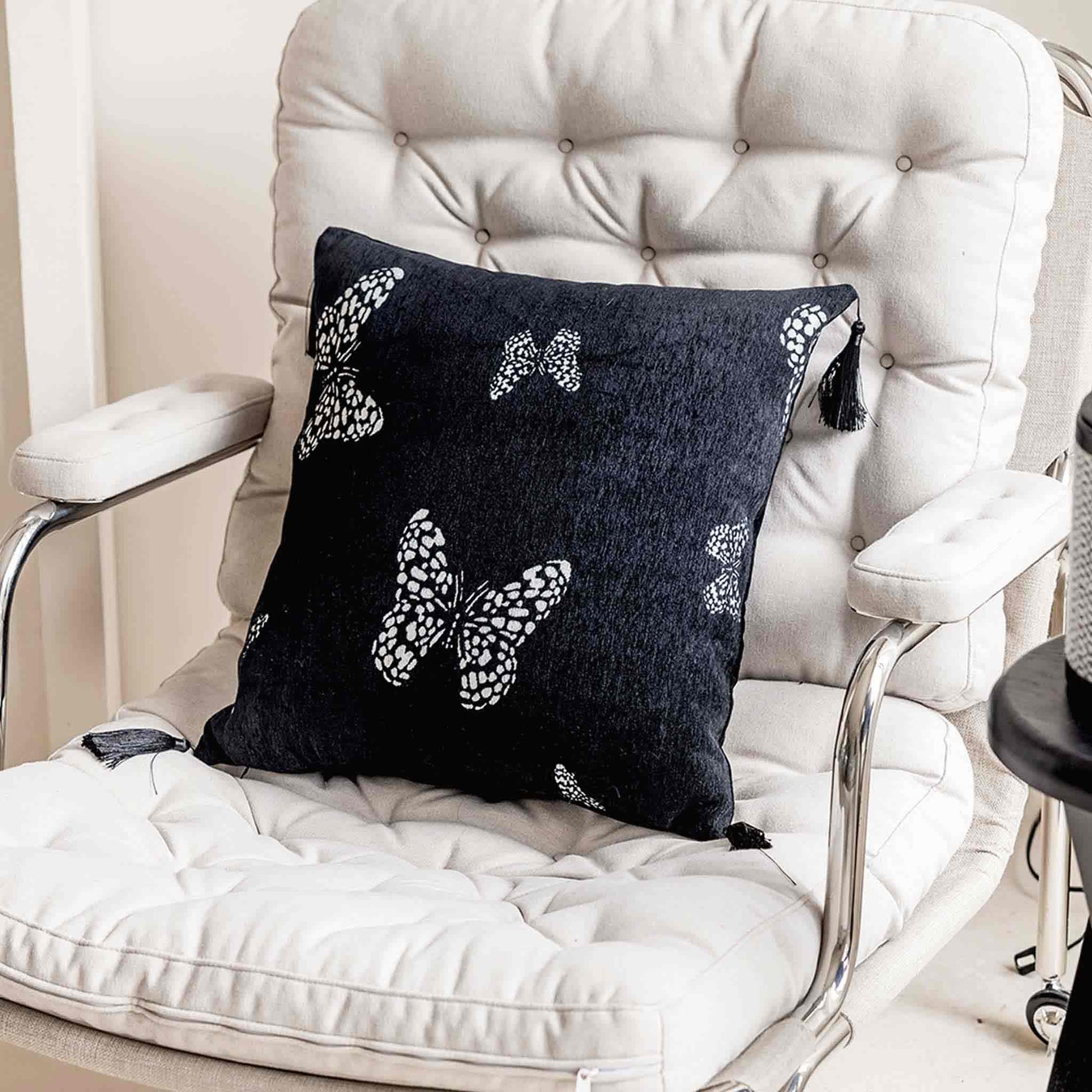 White butterfly on black background, fringed chenille cushion on chair.