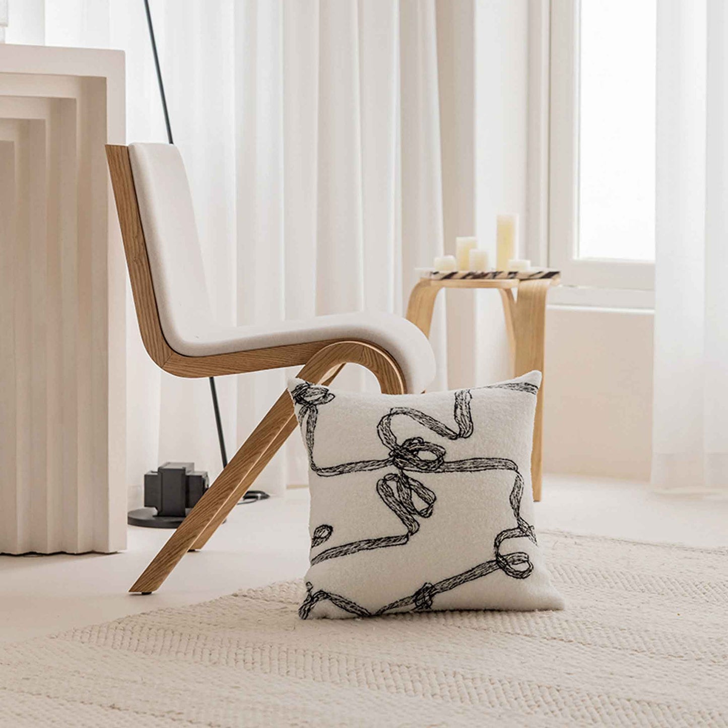 Modern wool cushion in a black and white ribbon pattern sit on the rug with a chair behind it.